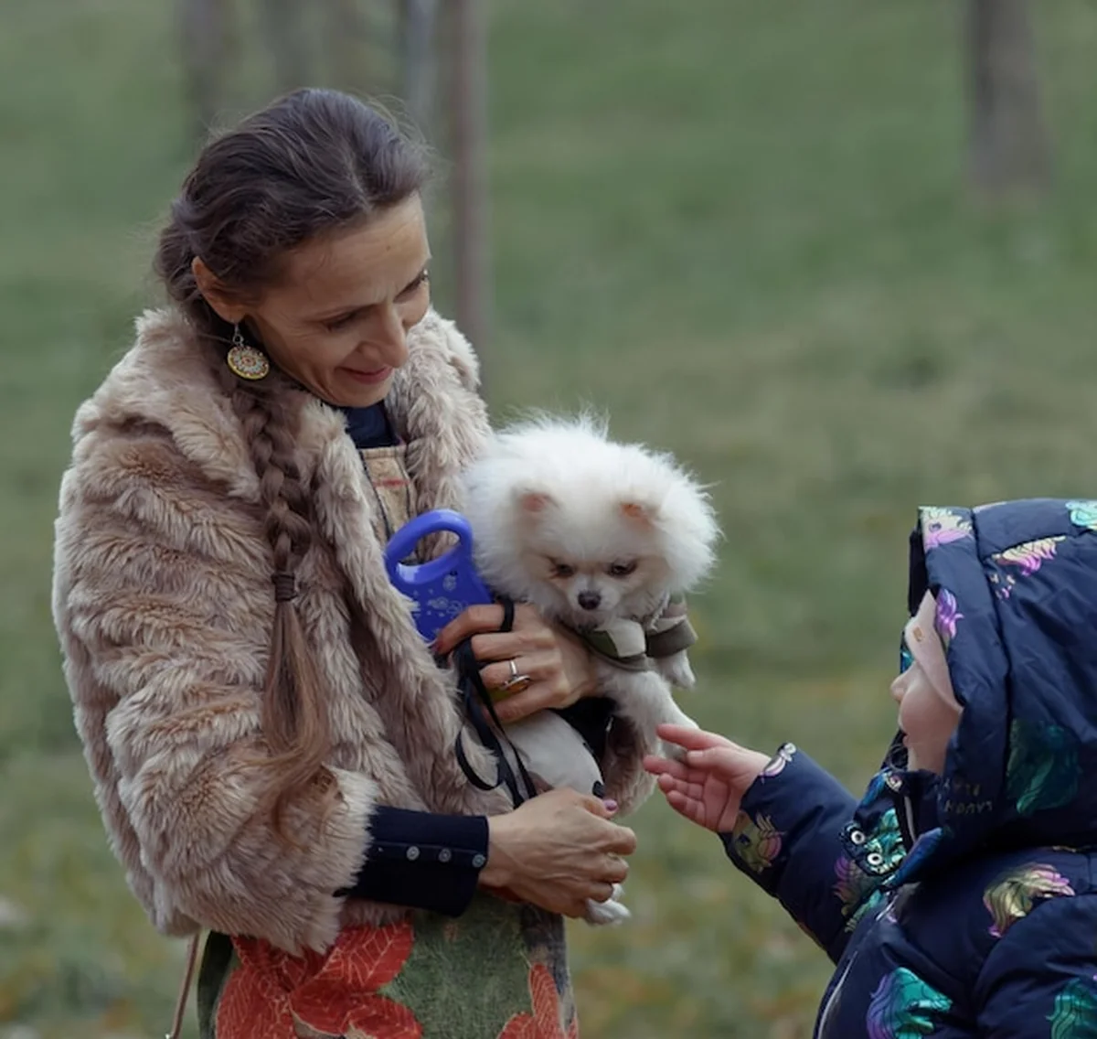 Kobieta trzyma psa, kobieta nosi futro z niebieską smyczką