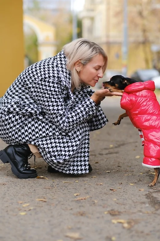 Kobieta w czerwonej kurtce bawi się z psem na świeżym powietrzu
