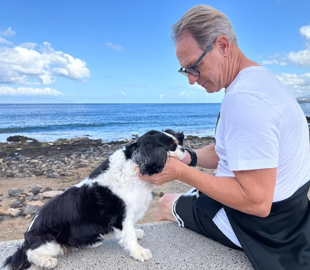 Starszy mężczyzna przytulający psa Cavalier King Charles na plaży