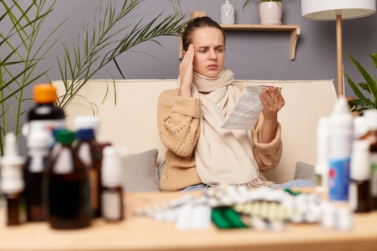 Młoda kobieta siedząca na kanapie w ciepłym swetrze czytająca instrukcje leku