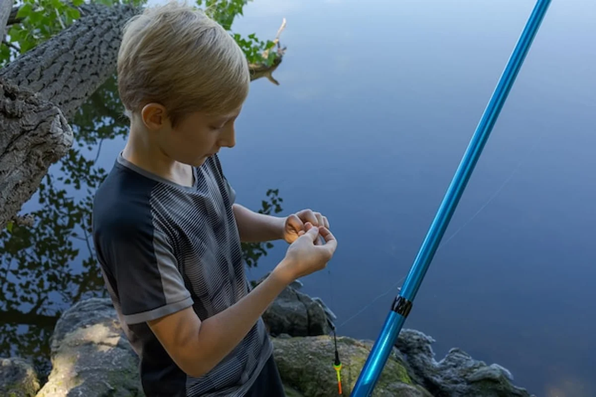 Młody wędkarz sprawdza przynętę na rzece latem